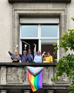 CSD Flagge auf dem Balkon der Geschäftsstelle gehisst, winkende Kolleg*innen