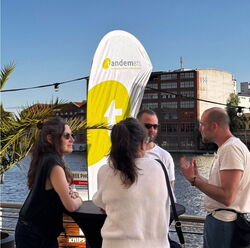 Vier Kolleg: innen tauschen vorm Beachflagge mit dem Logo von tandem BTL miteinander aus